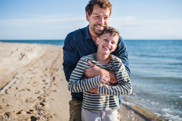 Father with small son hugging on a walk outdoors on beach, having fun.