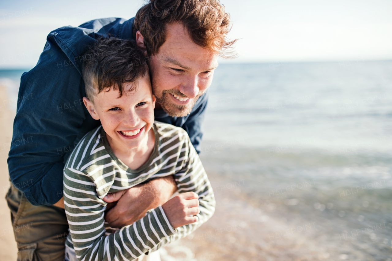 Father with small son hugging on a walk outdoors on beach, having fun.