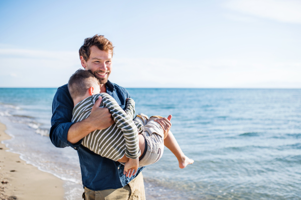 Father carrying small son on a walk outdoors on beach, having fun. Copy space.