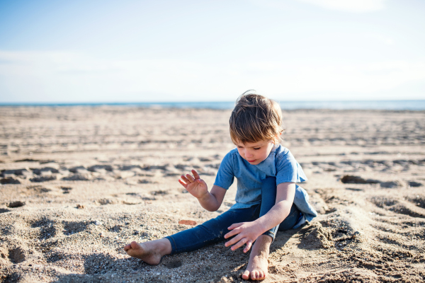 A happy small girl playing in sand outdoors on beach.