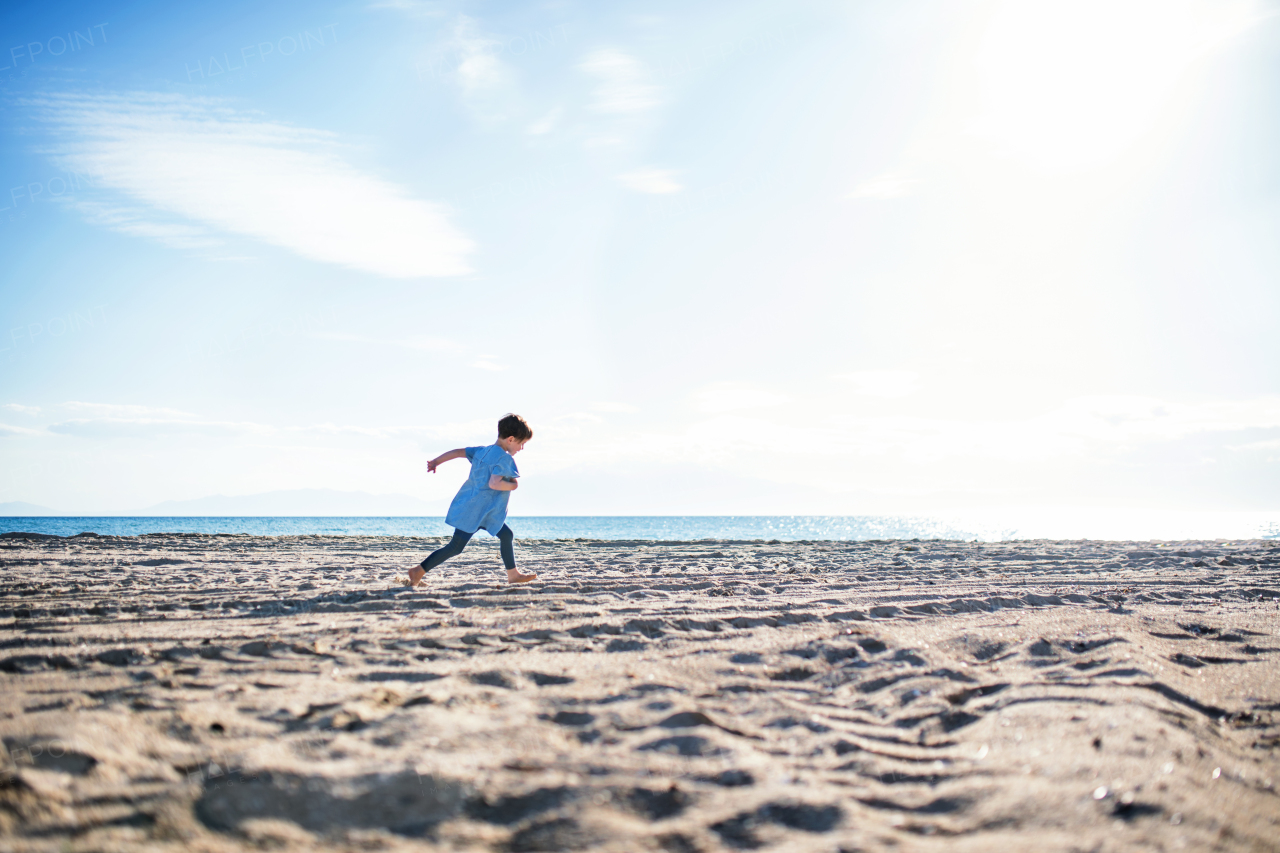 A small happy girl running outdoors on sand beach. Copy space.