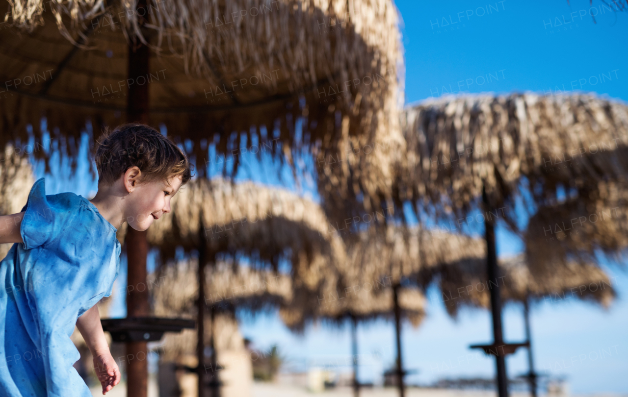 A small girl walking among straw parasols outdoors on beach. Copy space.