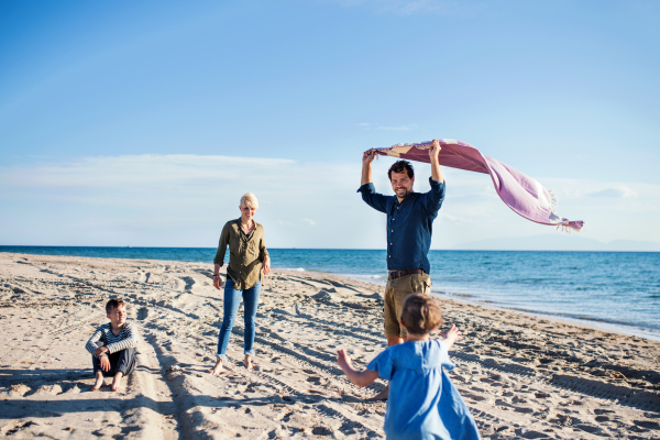 Young family with two small children walking barefoot outdoors on beach, having fun.