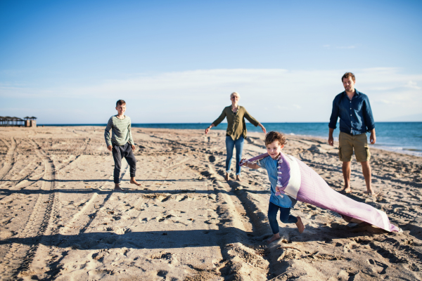 Young family with two small children walking barefoot outdoors on beach, having fun.