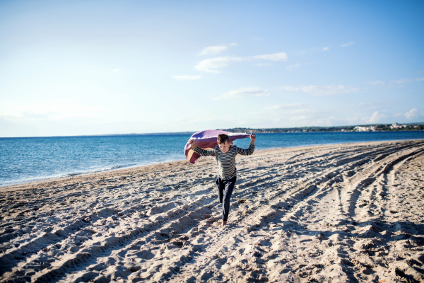 A small boy playing outdoors on sand beach, running.