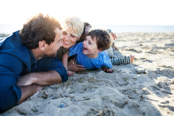 Portrait of young family with two small children lying down outdoors on beach, having fun.