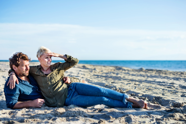 Happy young couple lying outdoors on sand beach, talking. Copy space.