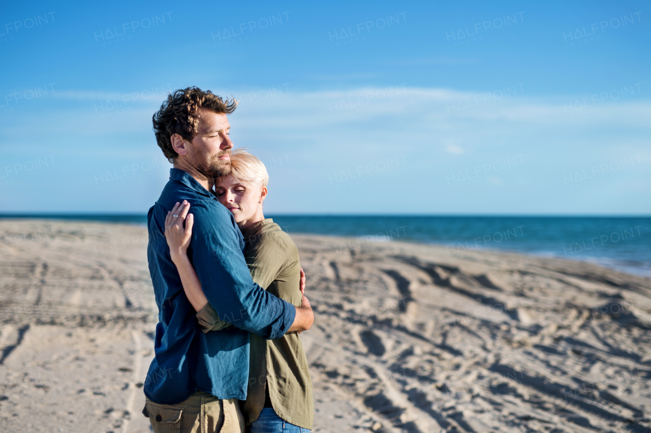 A young couple standing outdoors on beach, hugging. Copy space.