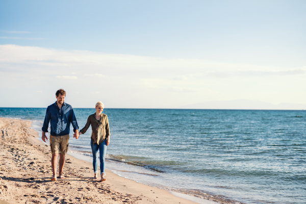 A young couple walking outdoors on beach, holding hands. Copy space.