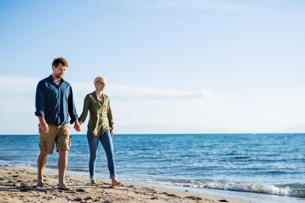 A young couple walking outdoors on beach, holding hands. Copy space.