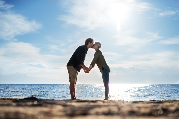 A young couple standing outdoors on beach, kissing. Copy space.