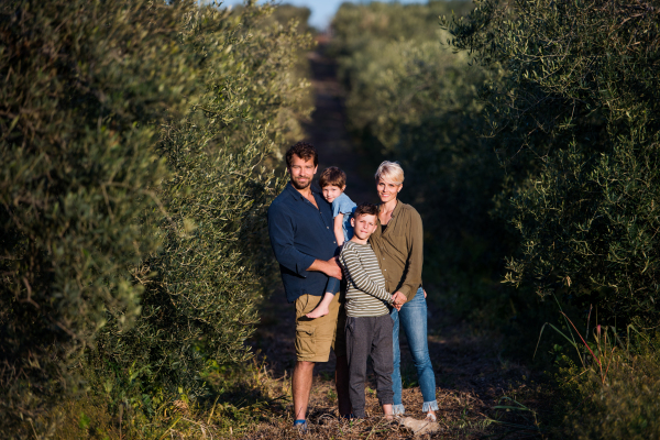 Front view of young family with two small children standing outdoors by olive trees.