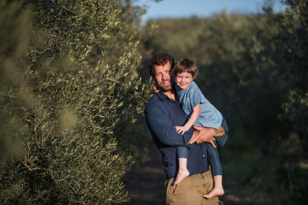 Portrait of father holding small daughter, standing outdoors by olive tree.