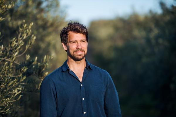 Front view portrait of mature man standing outdoors in olive orchard.