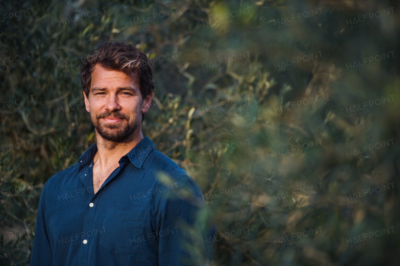 Handsome bearded man standing outdoors by olive tree. Copy space.