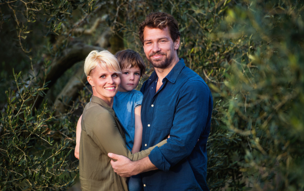 A portrait of young family with two small daughter standing outdoors by olive tree.