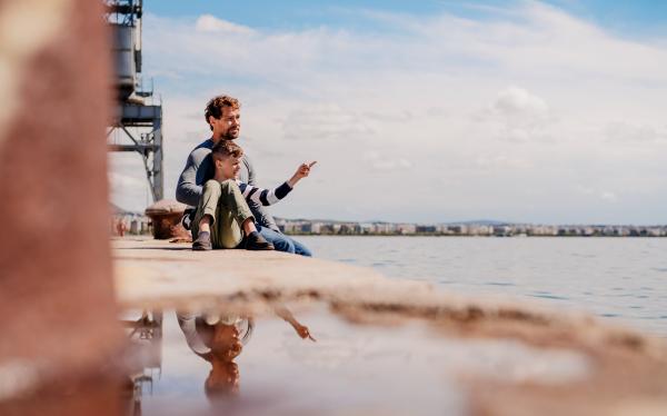 A father with small son sittting outdoors in town by the sea, talking.