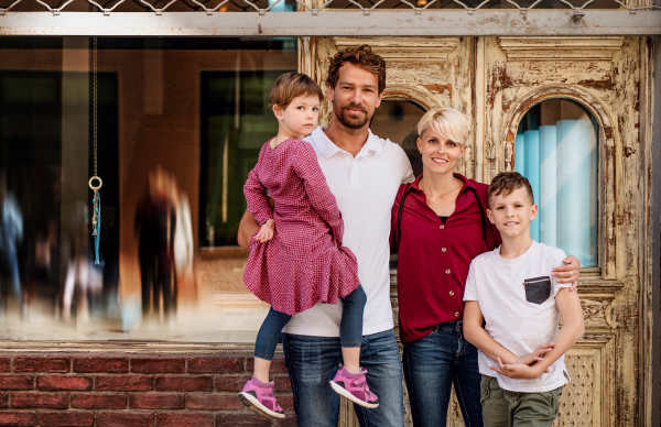 Front view of happy young family with two small children standing outdoors in town.