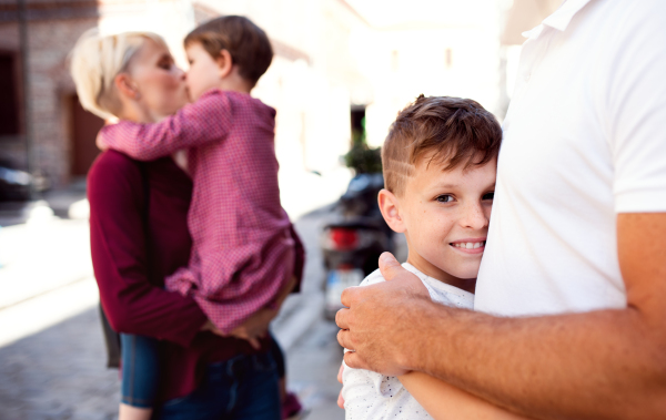 A midsection of young family with two small children walking outdoors in town.