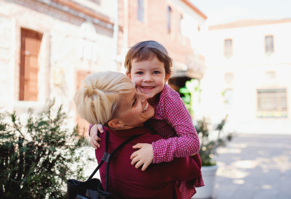 Mother with small daughter standing outdoors on street in mediterranean town, holding her.