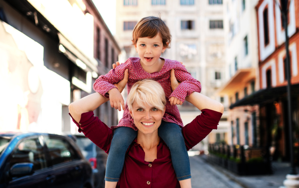 Father with small daughter standing outdoors on street in mediterranean town, giving a piggyback ride.