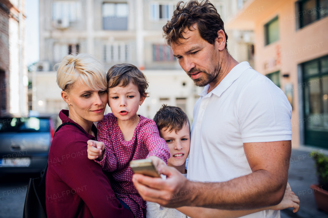 A young family with two small children standing outdoors in town, taking selfie with smartphone.