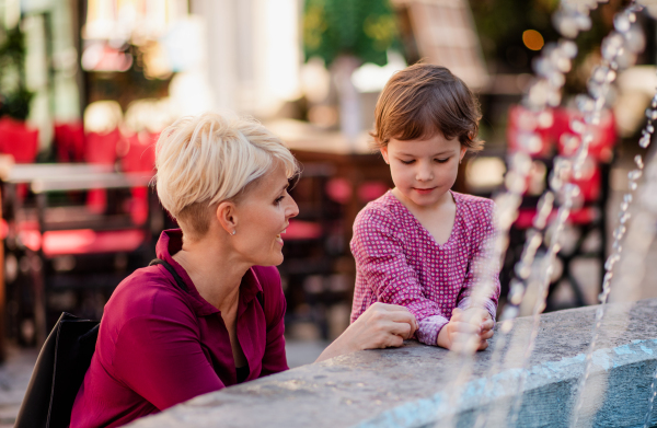 Mother with small daugther having fun by fountain outdoors in town on holiday.