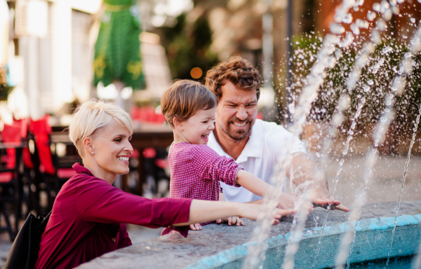 Parents with two small daugther having fun outdoors by fountain in town.