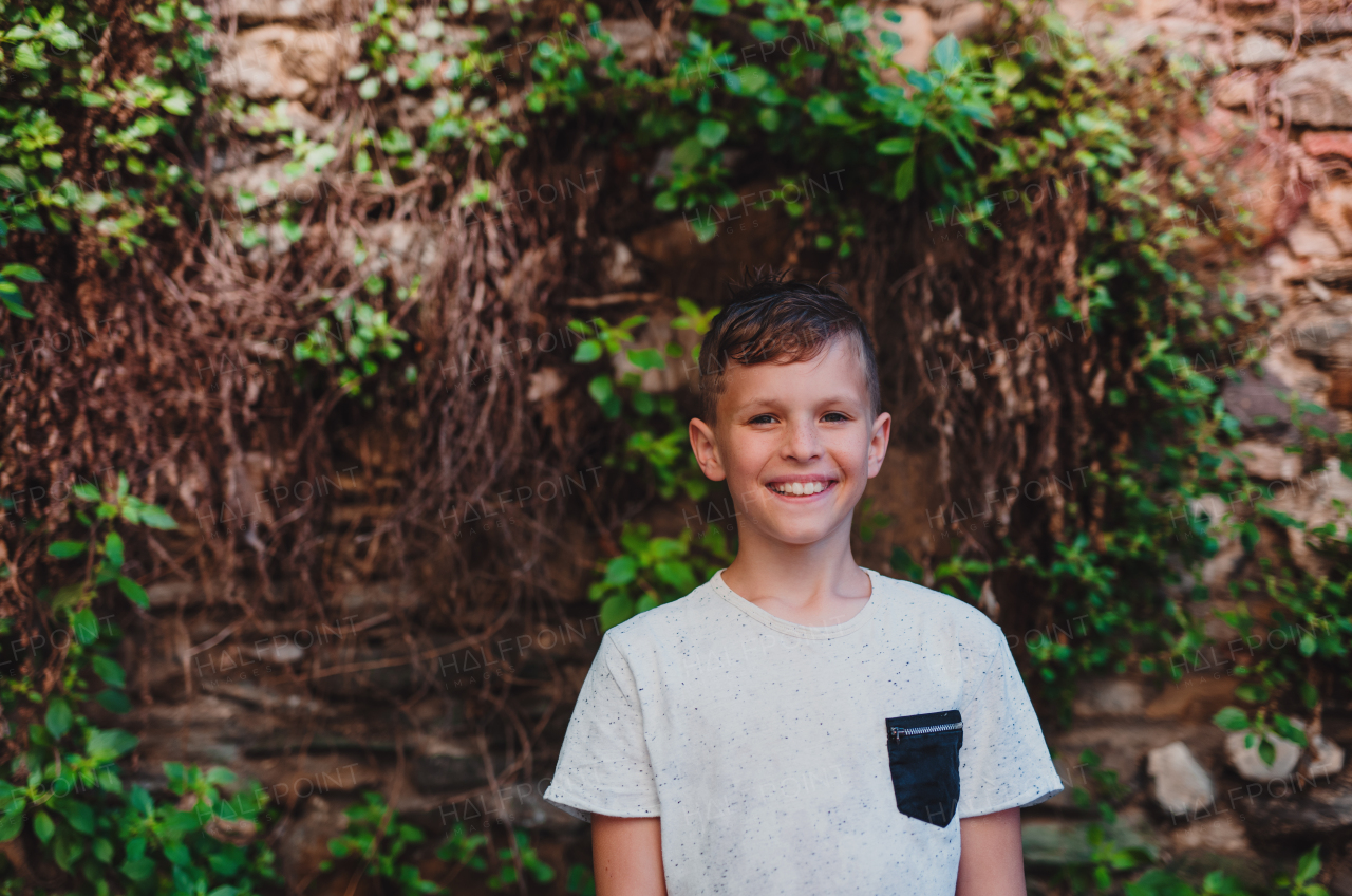 A portrait of small boy standing outdoors in front of old brick wall, looking at camera.