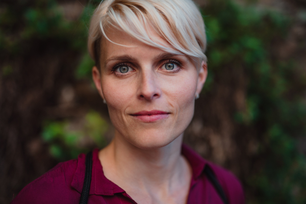 A close-up portrait of blond woman standing outdoors, looking at camera.