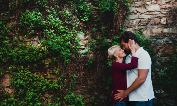 Young affectionate couple standing and hugging outdoors, a stone and green wall in the background. Copy space.