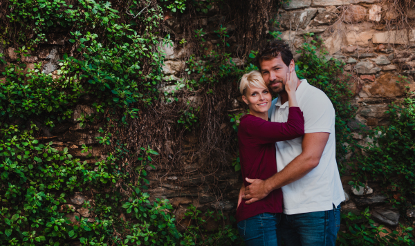 Young affectionate couple standing and hugging outdoors, a stone and green wall in the background. Copy space.