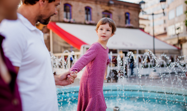 Parents with small daugther having fun outdoors by fountain in town.