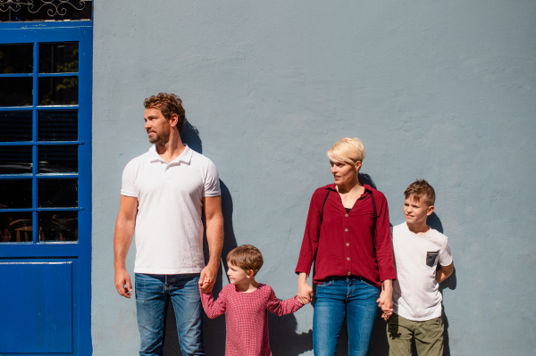 Front view of happy young family with two small children standing outdoors in town.