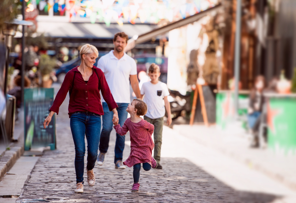 Happy young family with two small children walking outdoors in town on holiday, talking.