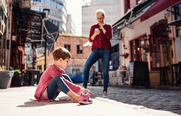 A small girl with a mother sitting outdoors on pavement, taking off shoes.