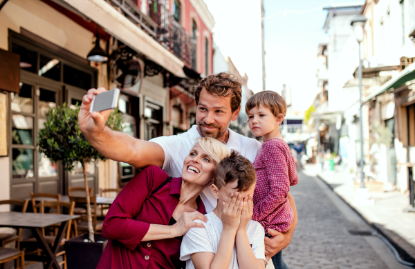 A young family with two small children standing outdoors in town, taking selfie with smartphone.