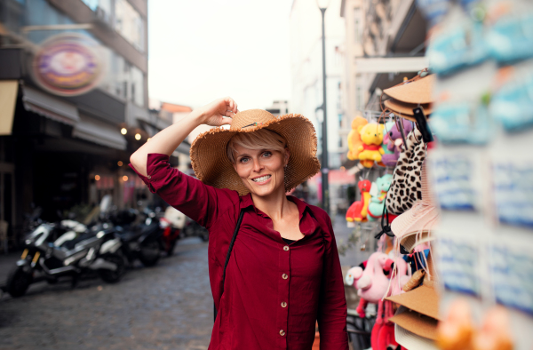 A young woman standing outdoors in town on holiday, trying on a hat.