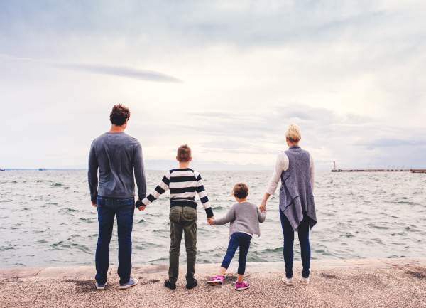 Rear view of young family with two small children standing outdoors on beach, holding hands.