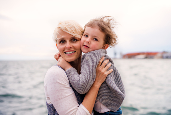 Front view of young mother with small daughter standing outdoors on beach.