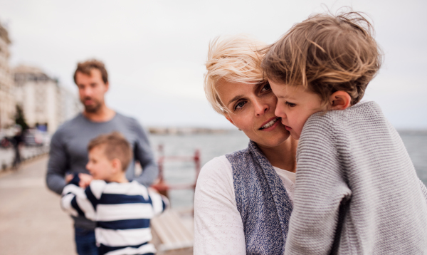 Young family with two small children outdoors on beach, looking at camera.