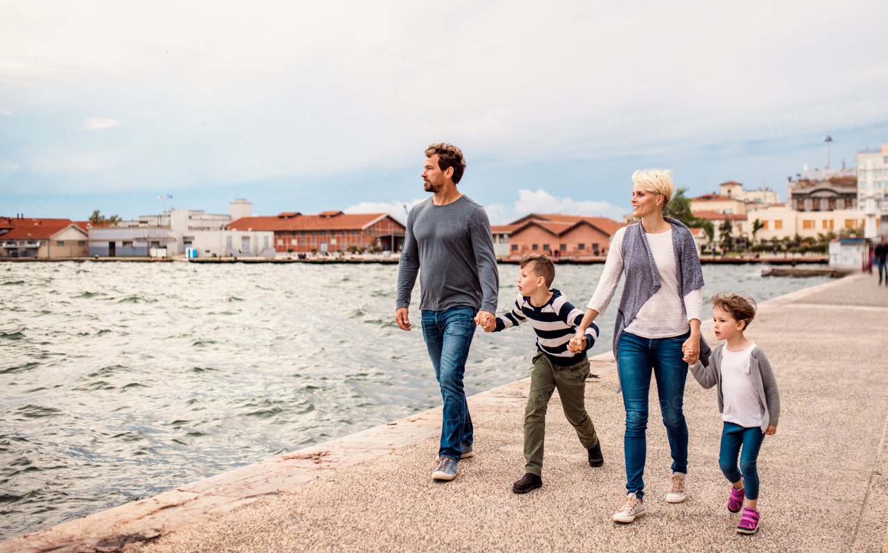 A young family with two small children walking outdoors on beach, holding hands.