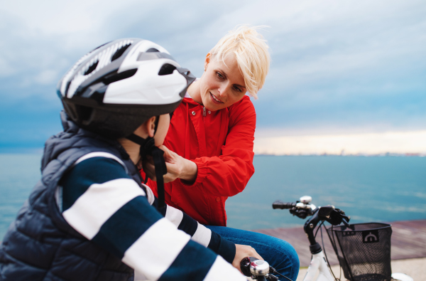 Mother and small son with bicycles outdoors standing on beach, talking.