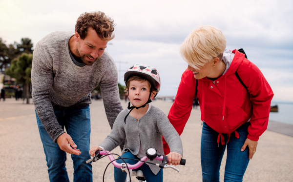 A young family and small daughter with bicycle outdoors on beach.