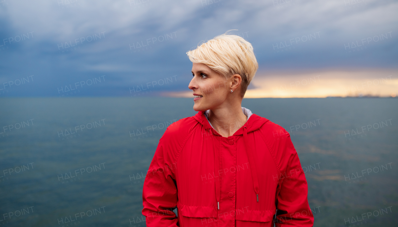 A portrait of young woman standing outdoors on beach at dusk. Copy space.