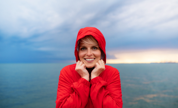 A portrait of young woman standing outdoors on beach at dusk, looking at camera.