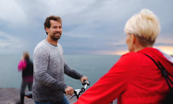 Happy couple with bicycles outdoors on beach, talking.