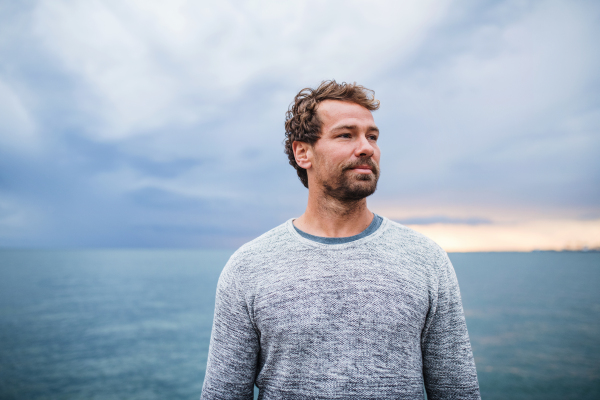 Portrait of mature man standing outdoors on beach at dusk.