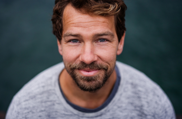 A portrait of happy handsome man standing outdoors, looking at camera.