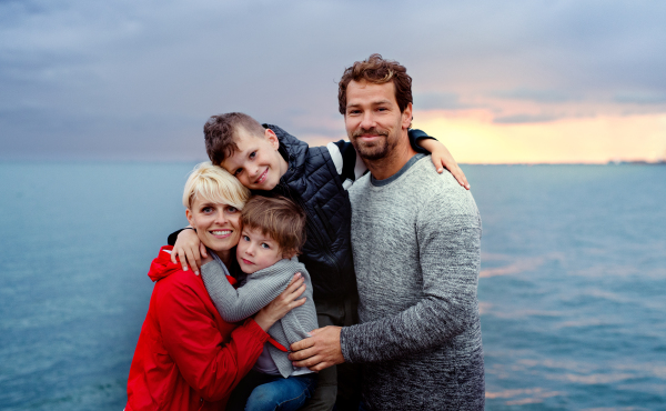 A portrait of young family with two small children outdoors on beach at dusk.